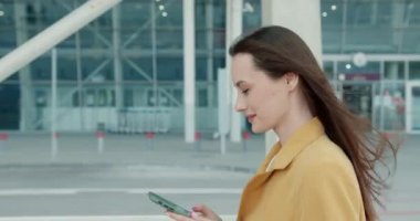 Kendine güvenen iş kadınlarının modern binanın yakınında ellerinde akıllı telefonuyla yürümeleri. Başarı, kariyer ve teknoloji kavramı. 