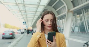 Sarı ceketli çekici bir iş kadını ciddi bir yüz ifadesiyle sokakta yürürken modern akıllı telefon kullanıyor. İnsanlar ve teknoloji kavramı. 