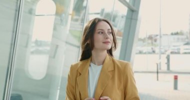 Aydınlatıcı ceketli genç bir kadın şehir merkezinde yürüyor ve modern akıllı telefon kullanıyor. İnternette iş meselelerini çözen pozitif iş kadını.