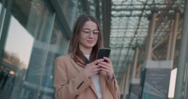 Kahverengi saçlı, caddede dikilen ve modern akıllı telefon üzerinde çalışan hoş bir bayan. Gözlüklü kadın yönetici Mesafe problemleri çözmekle meşgul.