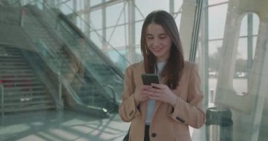 İş yerinde çalışan genç bir bayan ofis dışında modern akıllı telefon kullanıyor. Kahverengi saçlı güzel bir kadın modern cam binanın yanında duruyor ve cep telefonunda daktilo yazıyor..