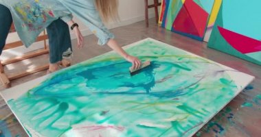 Uzun sarı saçlı, beyaz tuvalde fırçayla mavi boya uygulayan yetenekli bir kadın sanatçı. Genç bir kadın sanat stüdyosunda şaheser yaratıyor.. 