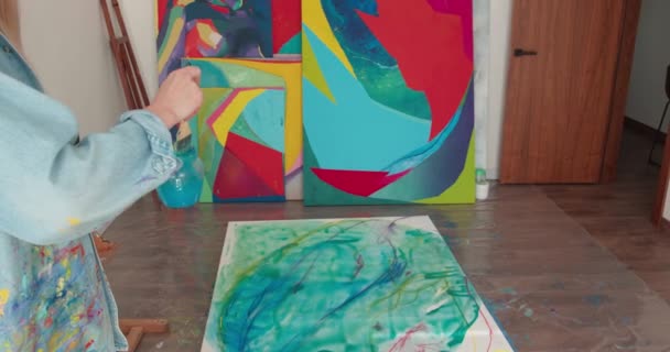 Inspirerad kvinnlig konstnär håller glas med vatten och rengöring pensel. Ung blond teckning på duk med färgglada färger och borste. Favorithobbykoncept. — Stockvideo