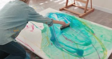 Sanat stüdyosunda yerde oturup tuvale resim çizen uzun sarı saçlı çekici bir kadın sanatçı. Çalışırken fırça ve renkli resimler kullanan genç bir kadın..