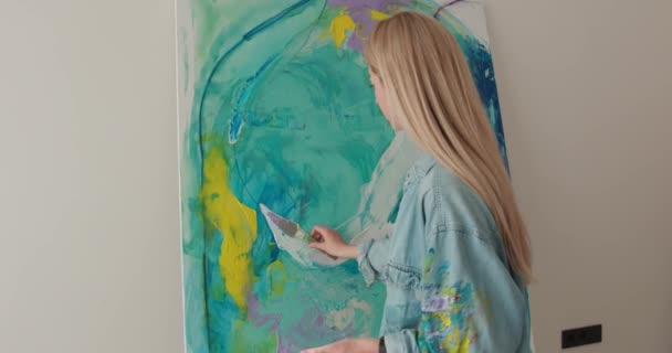 Widok tyłu kobiety blond malarstwo abstrakcyjny rysunek pędzlem i paletą kolorów w miejscu pracy. Terapia plastyczna w jasnym studio. Kreatywne hobby młodych ludzi. — Wideo stockowe