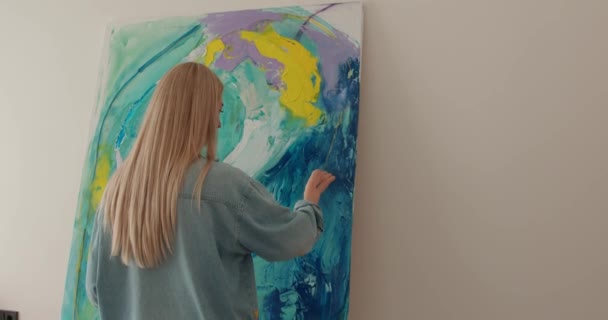 Artiste féminine talentueuse avec de longs cheveux blonds dessinant avec les doigts sur une grande toile. Peintre contemporain créant de l'art moderne abstrait au studio. — Video