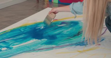 Yerde otururken fırçayla fırça çeken yetenekli kadın ressamlara yaklaş. Çalışma alanında genç sarışın soyut resim kalıpları.