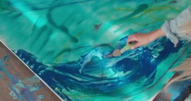 Sarı saçlı, renk paleti ve spatulayla tuvale çizen güzel bir genç kadın. Sanat stüdyosunda yerde oturan kadın sanatçı. Yaratıcılık kavramı. 