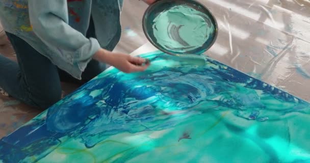 Close up of female artist using art palette and spatula for applying blue color on canvas. Skillful young woman creating abstract pattern at workplace. — Stockvideo