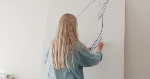 Back view of inspired young woman in casual outfit drawing on easel with brush and hand. Creative process at work. Enjoyment from art therapy. — Stockvideo