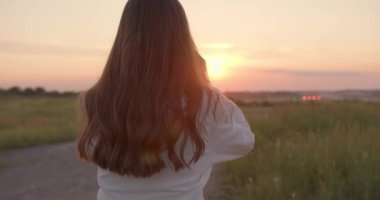 Kadın tarlada yürüyor ve dalgalı kahverengi saçlarına dokunuyor.