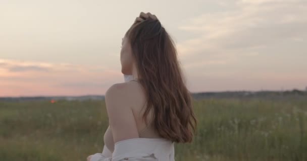 Vrouw in jurk wandelen op het platteland tijdens de zomer zonsondergang — Stockvideo