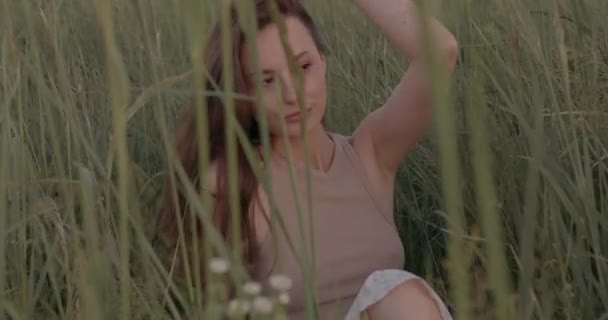 Tarlada çimlerin arasında oturan büyüleyici bir kadın — Stok video
