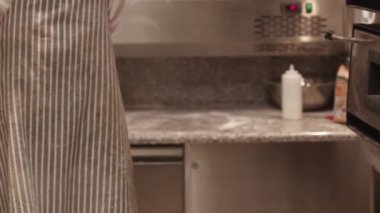 Önlüklü adam fırının içine pizza koyuyor.