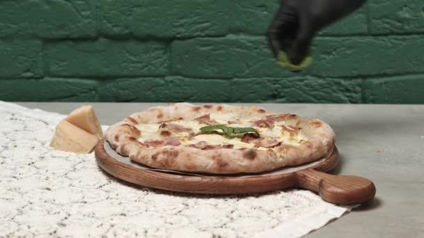 Mężczyzna w czarnych rękawiczkach rozkłada liście bazylii na pizzy — Wideo stockowe