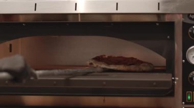Şef yemek pişirmek için sıra pizzayı fırına koyuyor.