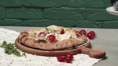 Siyah eldivenli bir adam pizza tabanına domates kirazı ekliyor.