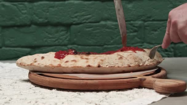 Крупный план мужских рук, разрезающих закрытую пиццу на борту — стоковое видео