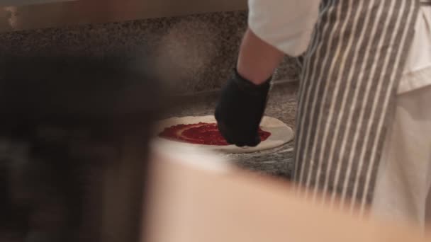 Chef in schort en handschoenen met tomatensaus op pizzadeeg — Stockvideo