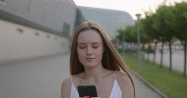 Mujer agradable caminando en la calle con el móvil en las manos — Vídeo de stock