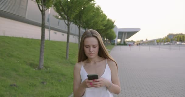 Młoda kobieta spacerująca ulicą i korzystająca ze smartfona — Wideo stockowe