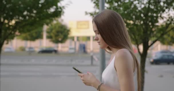 Widok z boku kobiety za pomocą smartfona podczas spaceru po ulicy — Wideo stockowe