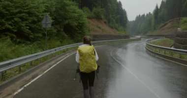 Dağların arasında ıslak yolda yürüyen genç bir kadın.
