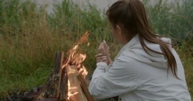 Yanan ateşin yanında oturan ve elleri ısıtan kadın.