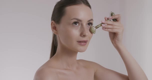 Pleasant model with bare shoulder using facial stone roller — Stock Video