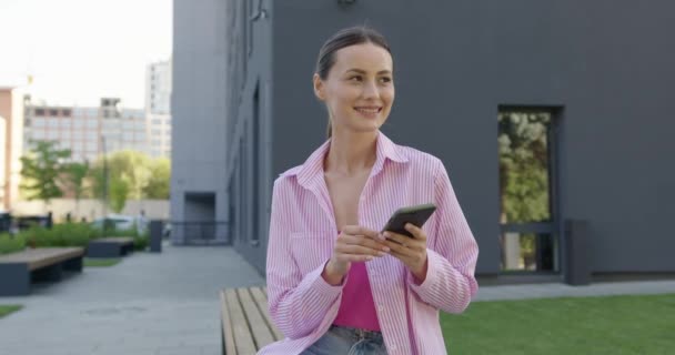 Charming woman sitting on bench with mobile in hands — Stock Video