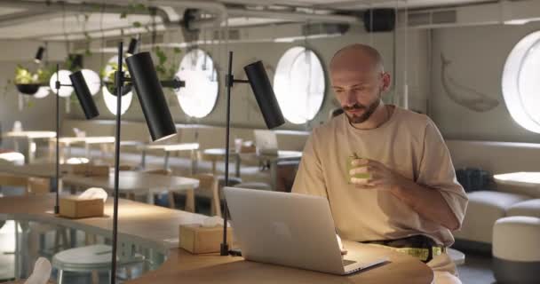 Junger bärtiger Mann sitzt im Café und arbeitet am Laptop — Stockvideo