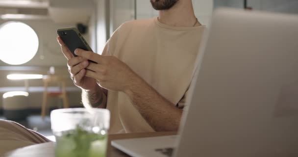 Nahaufnahme eines Mannes, der mit Smartphone und Laptop im Café sitzt — Stockvideo