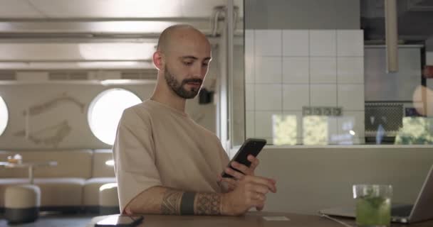 Hombre feliz sentado en la cafetería con ordenador portátil y teléfono inteligente — Vídeos de Stock