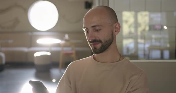 Bonito jovem sentado no café e usando smartphone — Vídeo de Stock