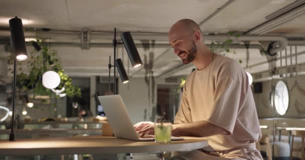 Seitenansicht eines lächelnden Mannes, der im Café auf dem Laptop tippt — Stockvideo