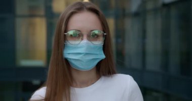 Yüz maskesi takmış caddede duran beyaz kadın portresi.