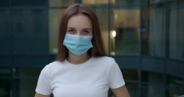 Dışarıda poz veren genç bir kadın tıbbi maske takıyor. 