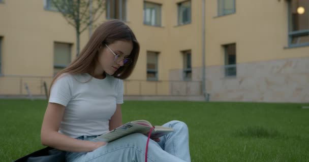 Mooie vrouw zitten op gras en het lezen boek — Stockvideo