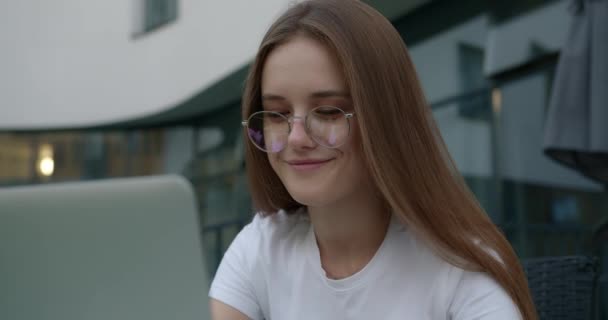 Estudiante feliz en anteojos escribiendo en el ordenador portátil al aire libre — Vídeo de stock