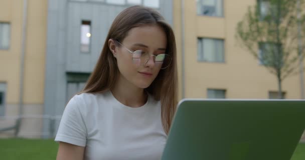 Красива жінка сидить на траві і використовує ноутбук для навчання — стокове відео