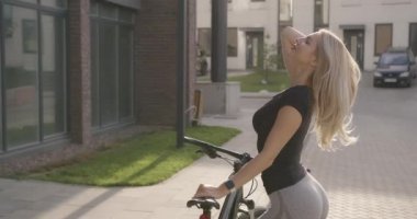 Spor kıyafetli güzel sarışın dışarıda bisiklet sürdükten sonra rahatlıyor.