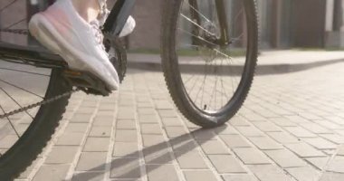 Dışarıda siyah bisikletle pedal çeviren kadın bacaklarını kapat.