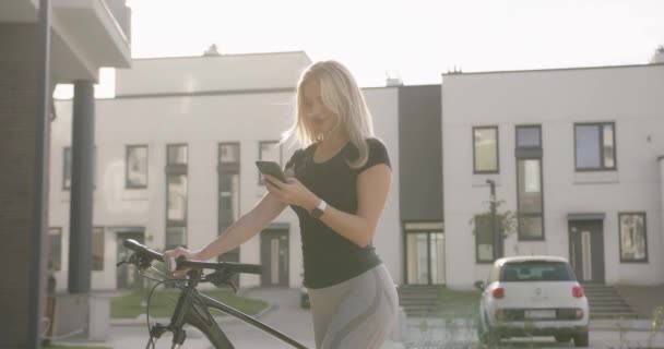 Mulher usando celular enquanto está de pé com bicicleta na rua — Vídeo de Stock