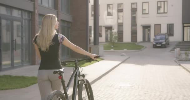 Vista trasera de la mujer fitness caminando con bicicleta en el área urbana — Vídeo de stock