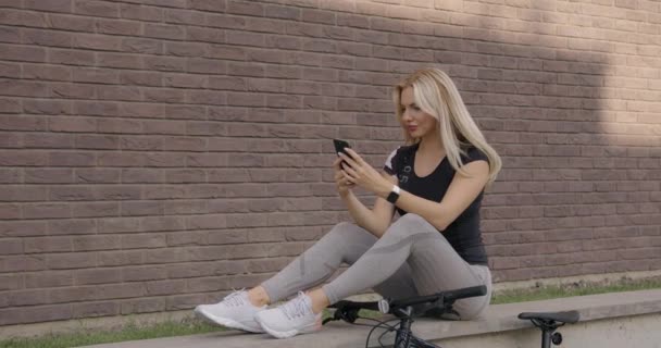 Mulher em sportswear descansando após o ciclismo e usando celular — Vídeo de Stock