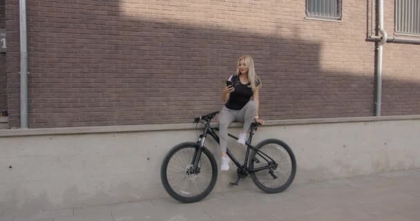 Mujer sentada en bicicleta y sosteniendo el teléfono celular al aire libre — Vídeo de stock
