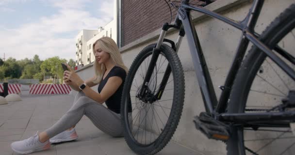 Mujer sentada en la calle cerca de la bicicleta y usando smartphone — Vídeo de stock