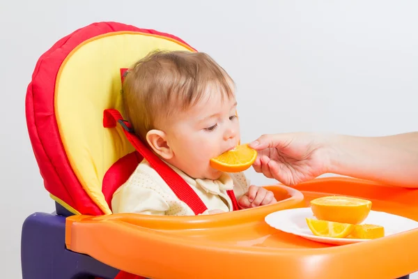 Baby zit in kinderstoel met sinaasappel. — Stockfoto