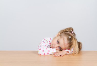  küçük kız masada ahşap yüzey üzerinde kafa dinlenme.