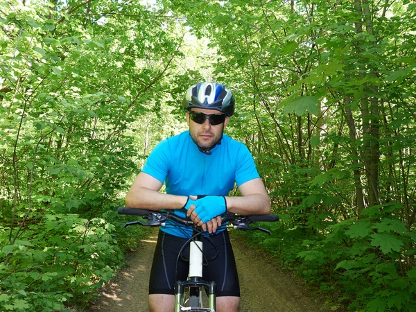 man riding a mountain bike in the green woods.